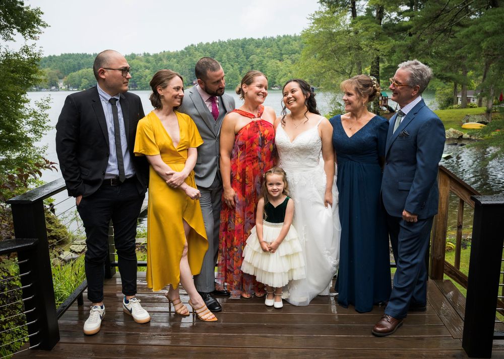 Wedding party sitting together in a candid moment on a wooden dock by a lake.