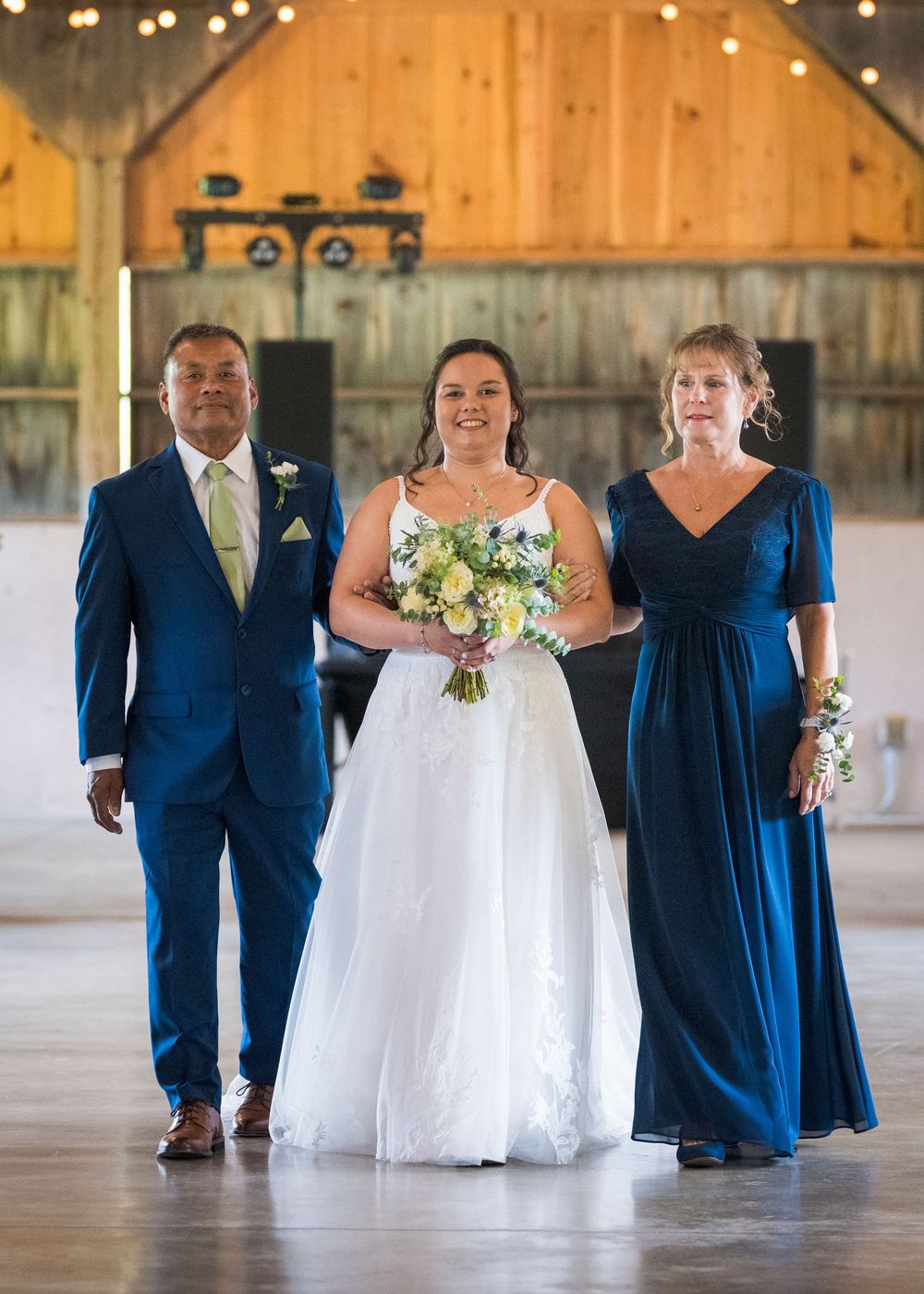 Wedding party in navy blue and white attire walks across wooden barn floor during reception.