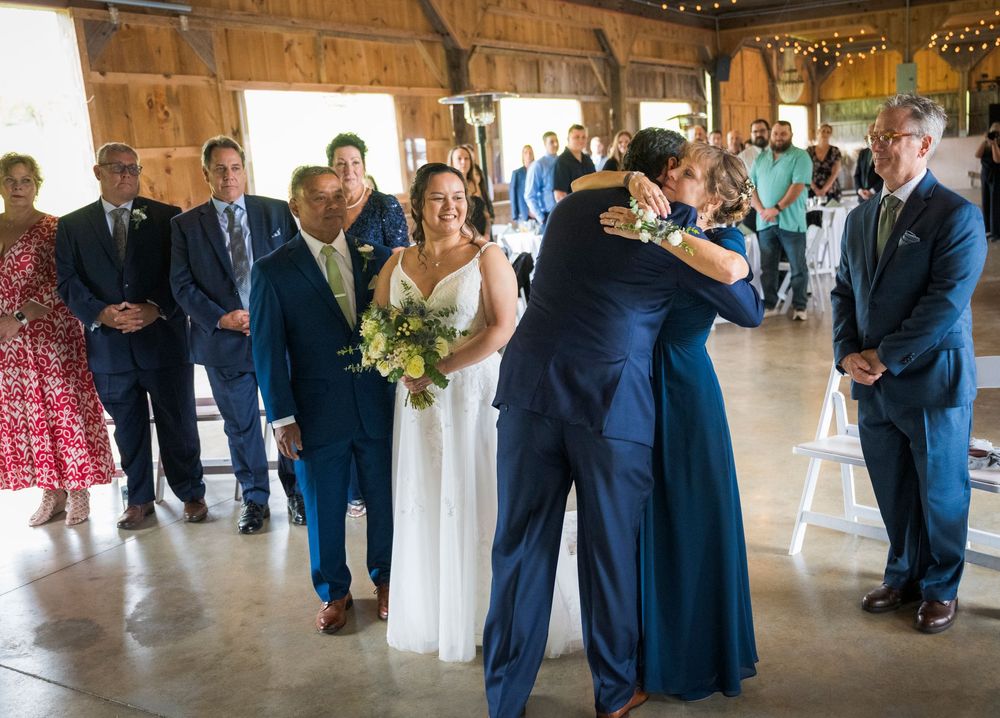 Wedding guests gather inside a rustic barn venue with string lights overhead.