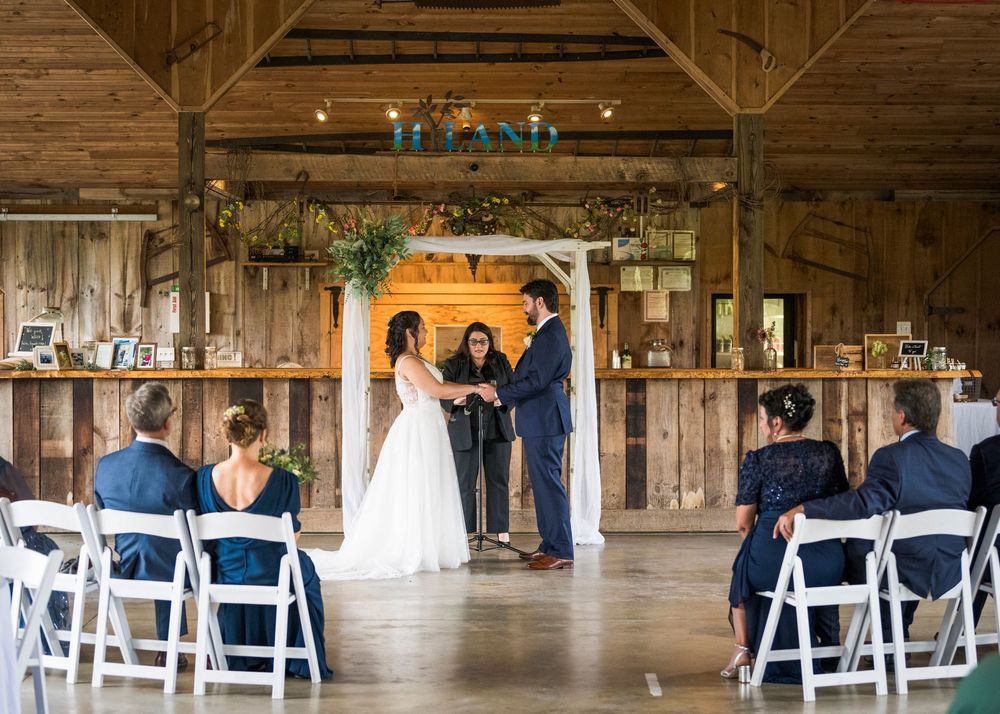Wedding reception setup inside rustic barn venue with white chairs and string lights hanging overhead.