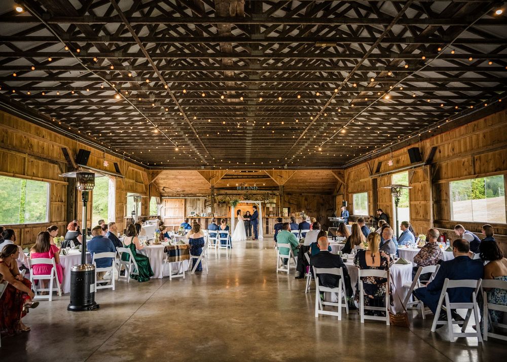 Rustic barn reception venue with twinkling string lights and white chairs set up for wedding celebration.