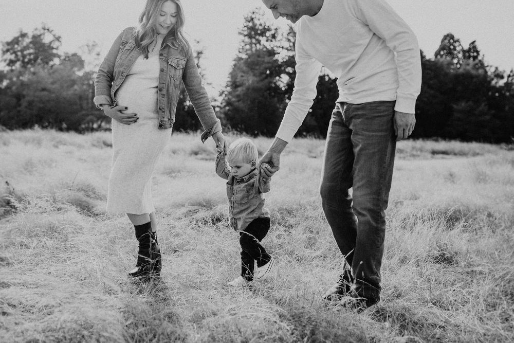 A family holds hands and walks through a grassy meadow on a sunny day in black and white.
