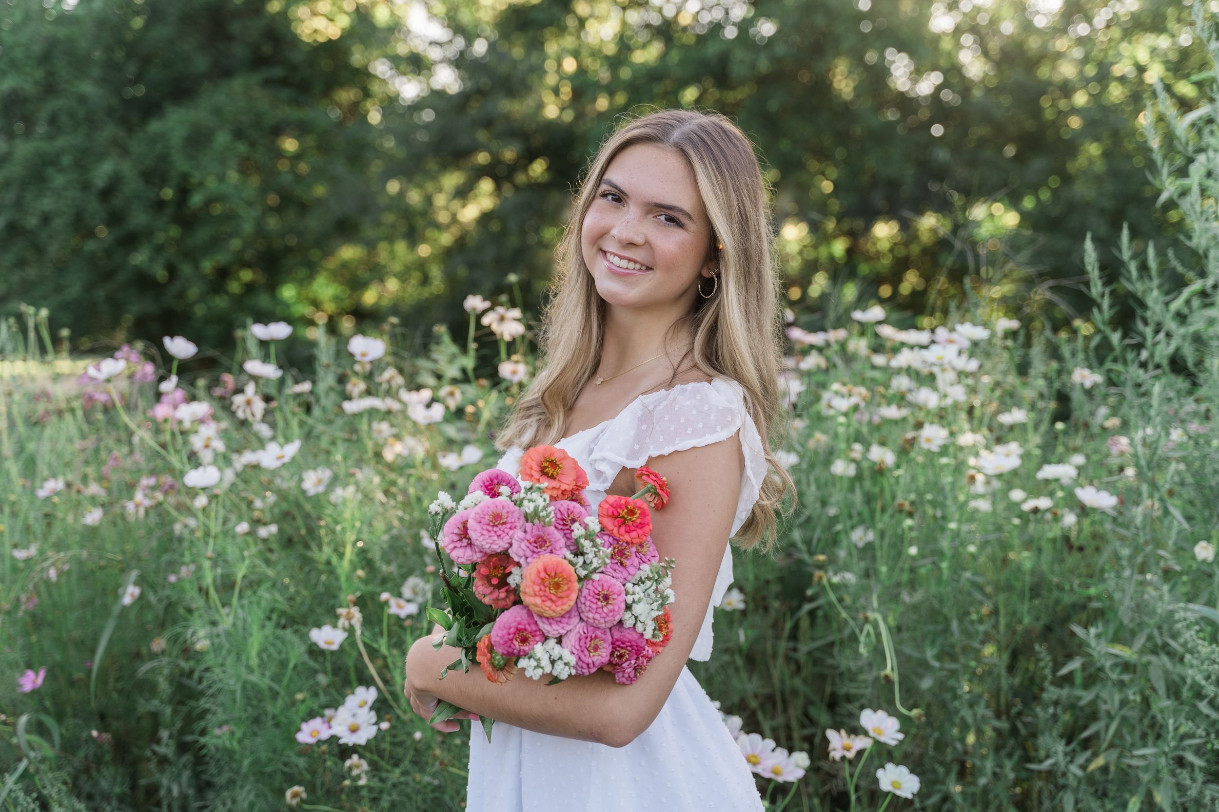 A person carries a bouquet of pink flowers while standing in a lush garden during golden hour.