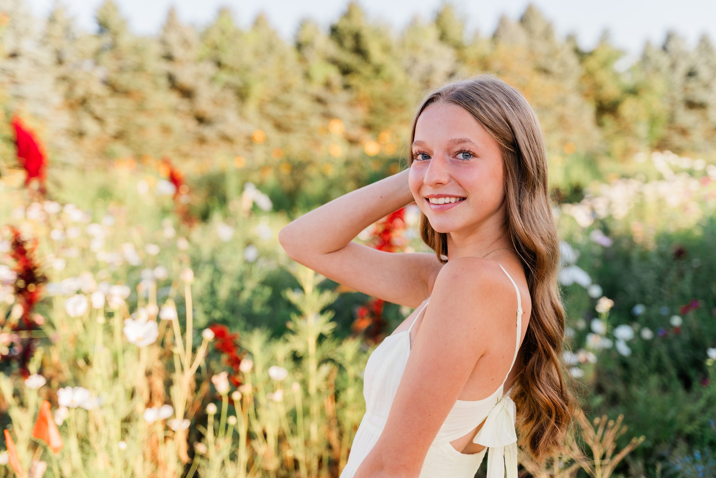 A person smiles while posing in a sunny meadow with wildflowers during golden hour.