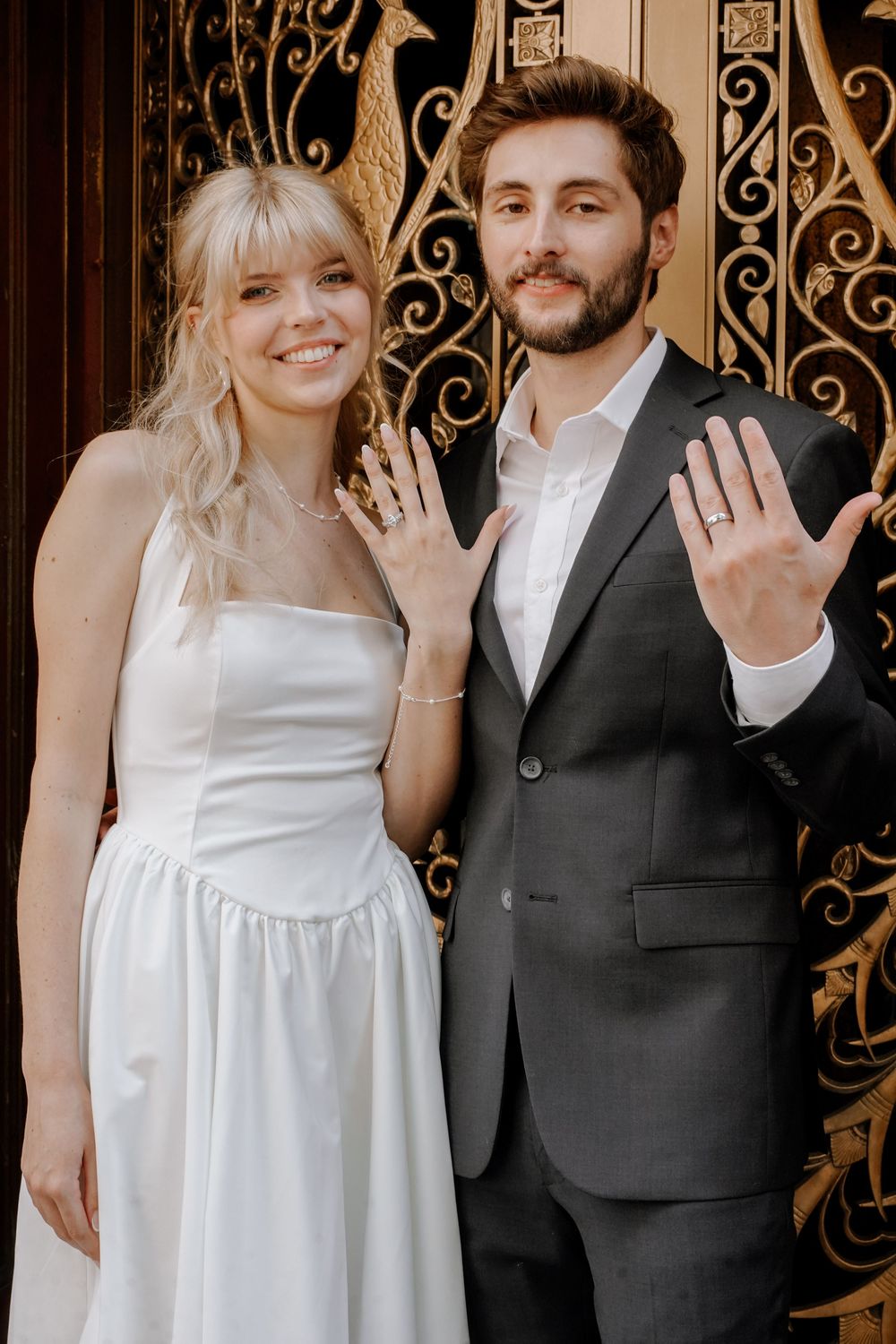 A couple displays their wedding rings in front of an ornate iron gate in multiple romantic poses.