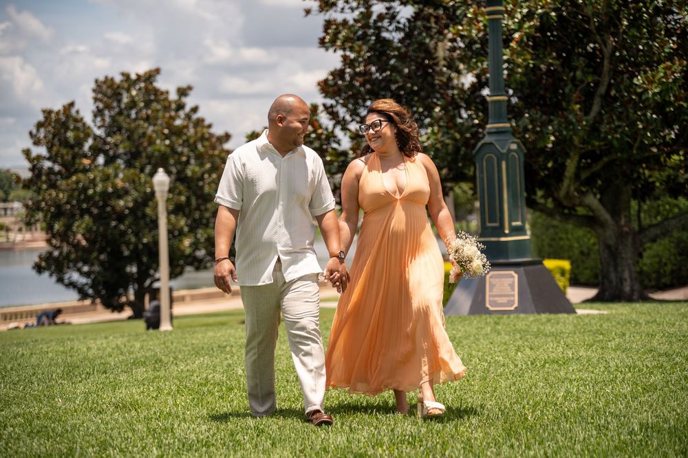 Engagement couple walking hand in hand on grassy lawn near waterfront, romantic photoshoot in Tampa, Florida with flowing peach dress.