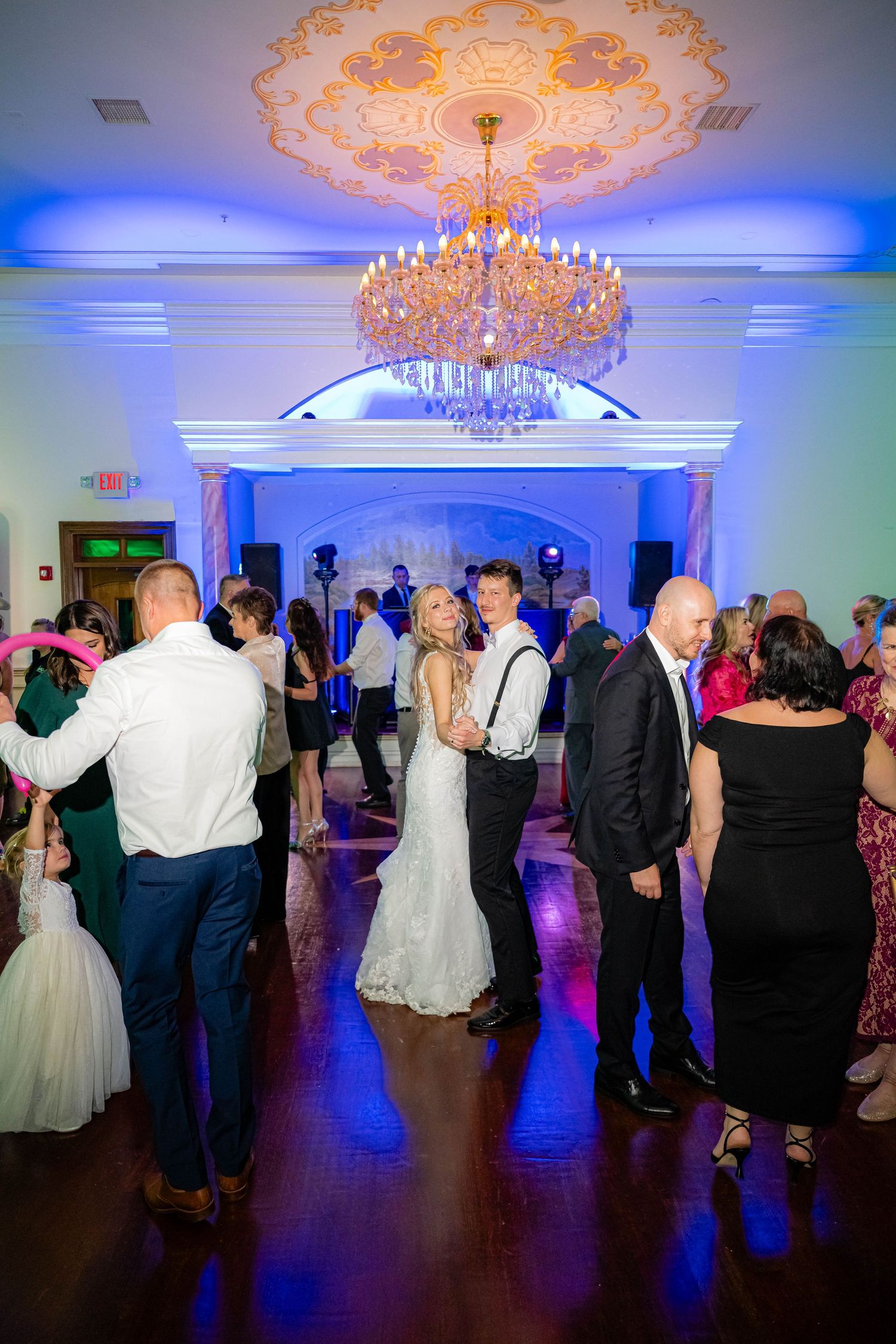 A crowded dance floor filled with people enjoying themselves under warm pendant lighting at a social event.