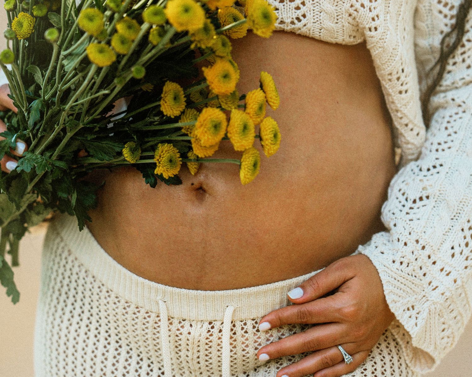 Close-up of a pregnant belly with yellow flowers against white knit clothing.