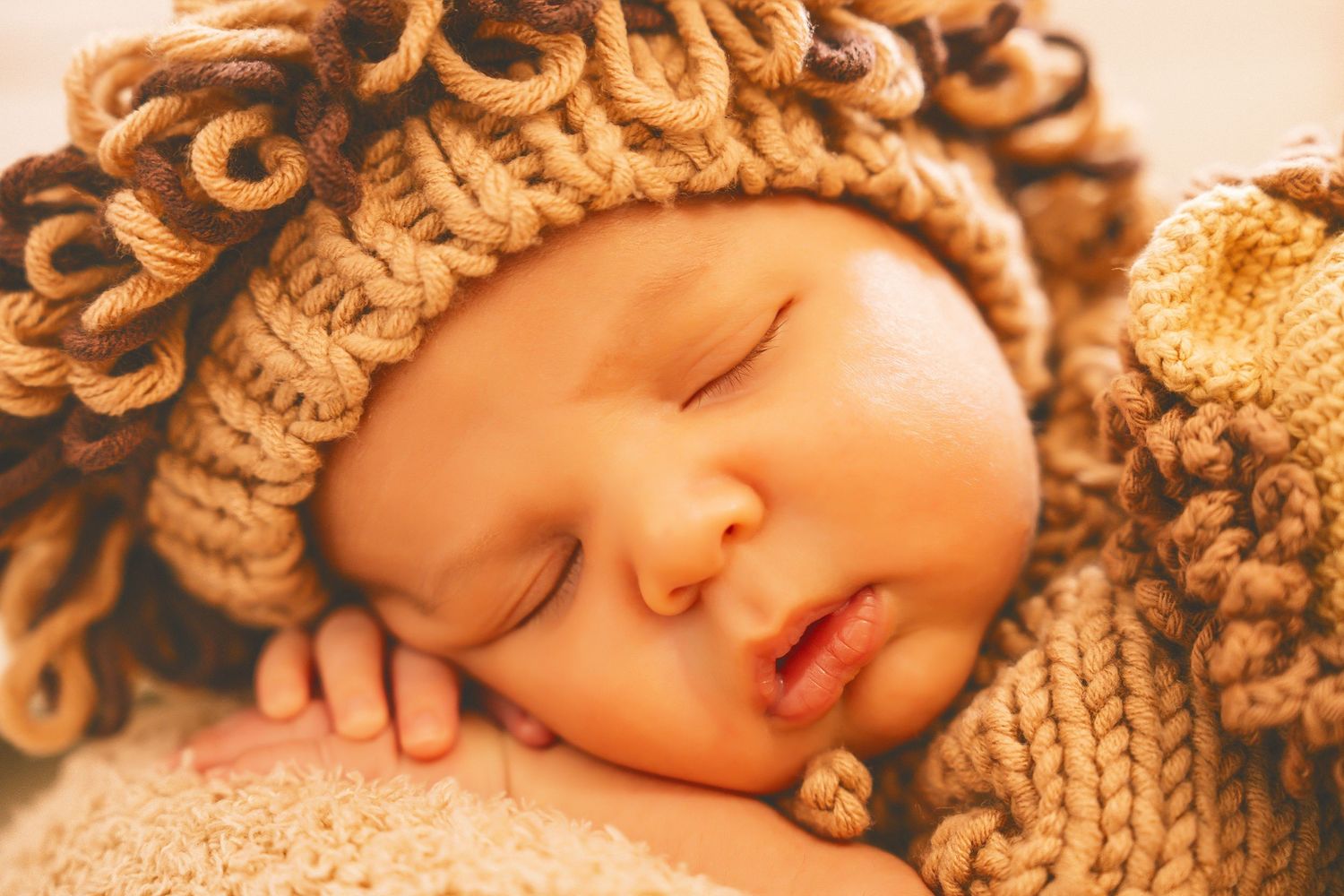 Peaceful sleeping newborn wearing brown knitted hat in warm tones.