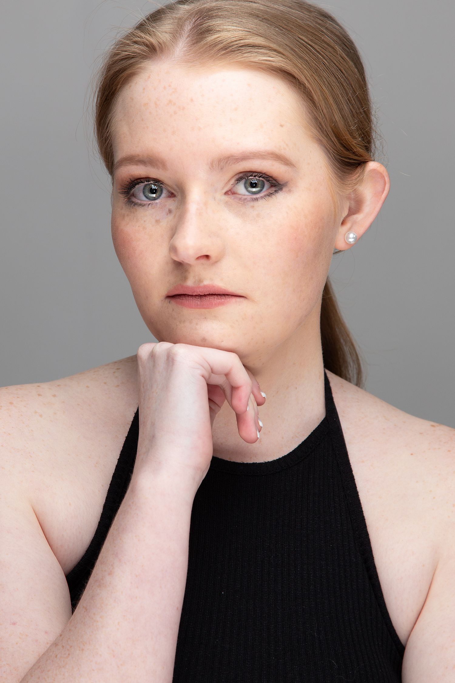 Professional portrait of woman in black halter top with natural makeup posing against gray background.