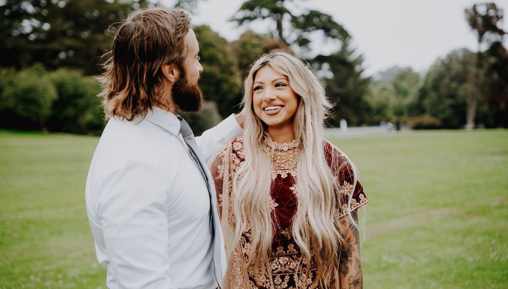 A couple shares a joyful moment together on a lush green lawn wearing boho-inspired outfits on a sunny day.
