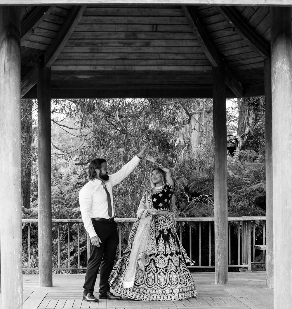 A couple in vintage attire dance together on a covered wooden gazebo porch in black and white.