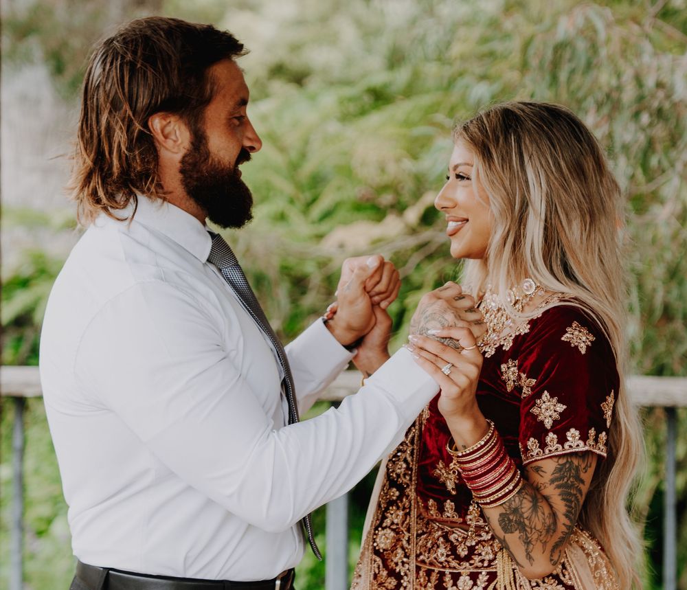 A couple shares a joyful moment outdoors, with one person wearing traditional embroidered red attire.