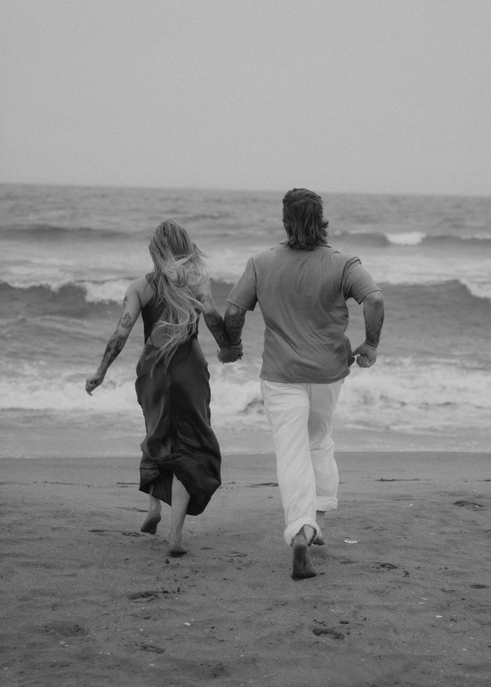 People running together joyfully along a misty beach shore in black and white.