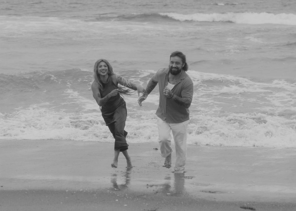 Black and white image of two people joyfully running and playing in the ocean waves at the beach.