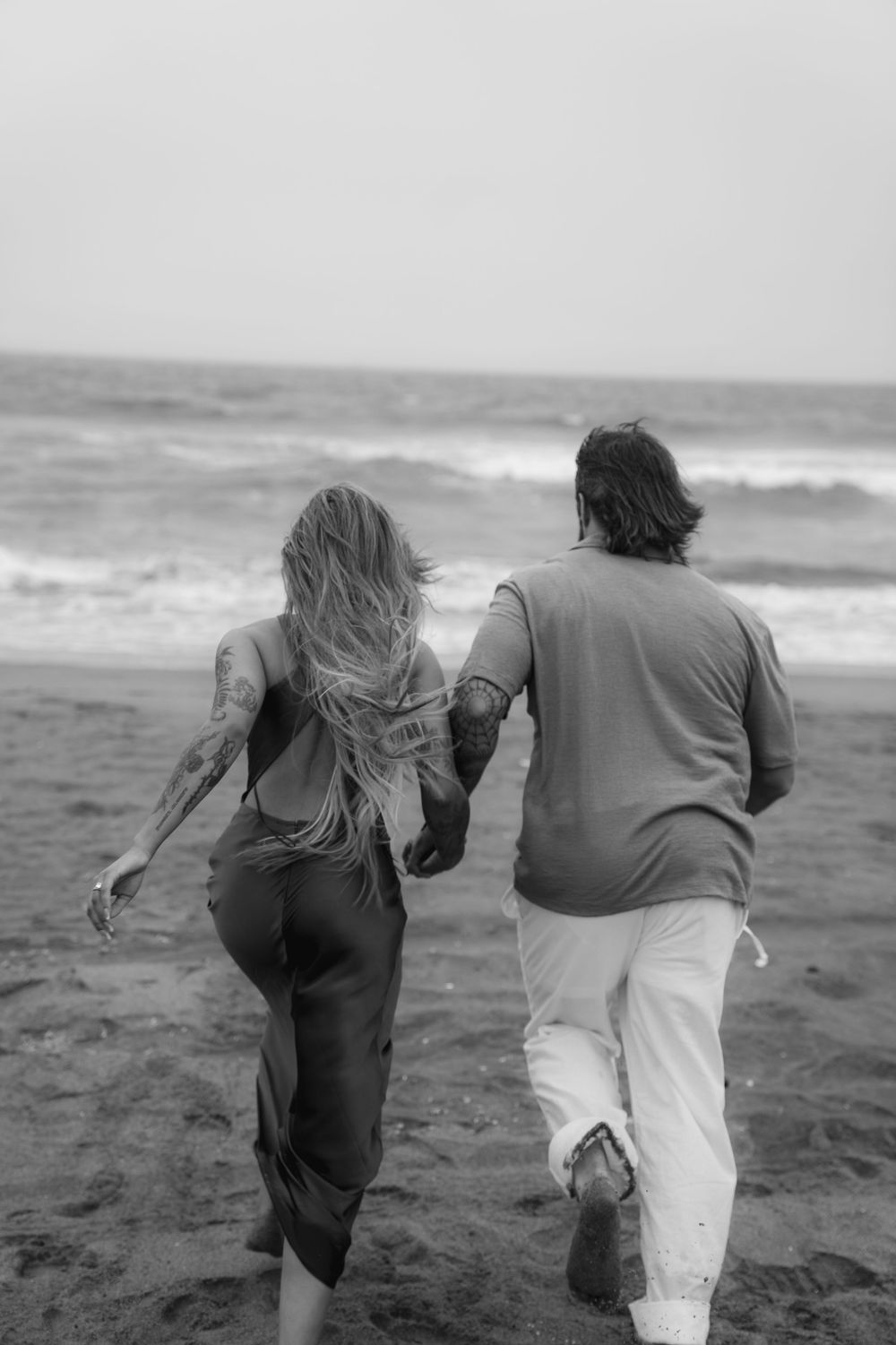 Two people running together on a misty beach with waves crashing in the background.