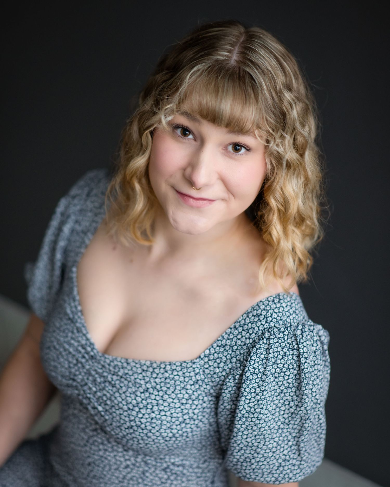 Portrait in soft lighting wearing a gray patterned dress against dark background.