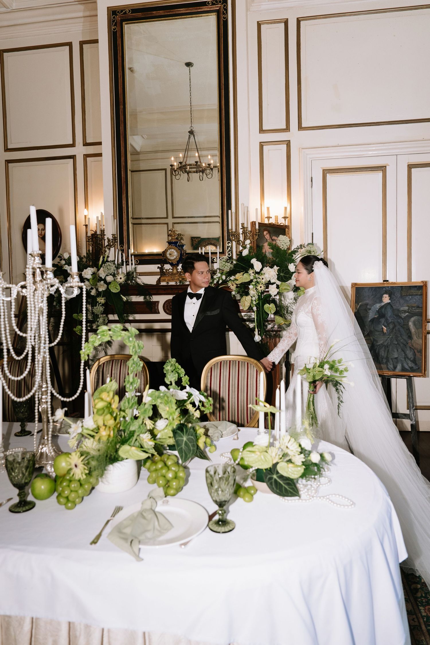 Wedding couple holds hands at a beautifully decorated sweetheart table with green floral arrangements and candelabras.