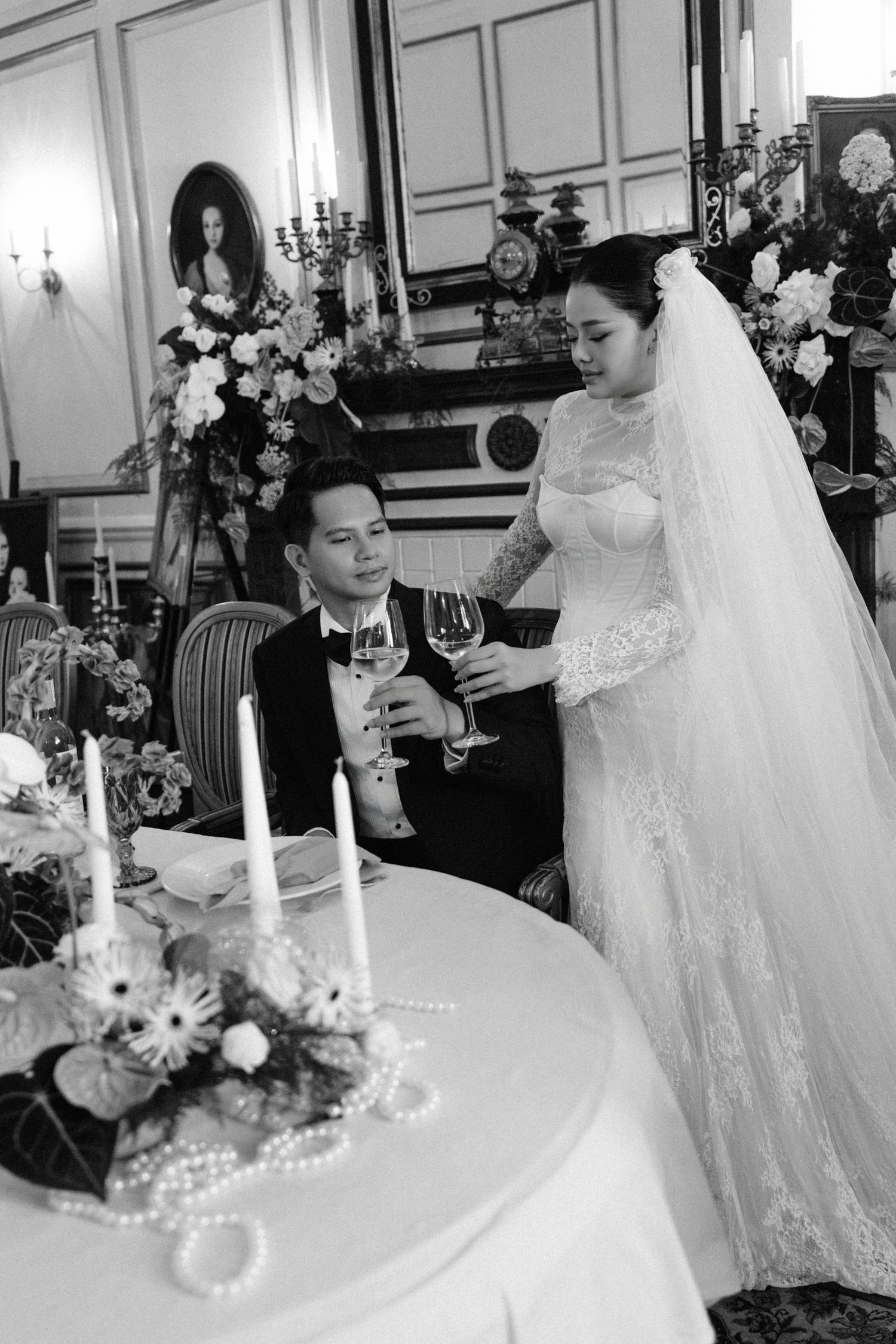 Black and white photo of bride and groom toasting with champagne glasses at a candlelit wedding reception table.