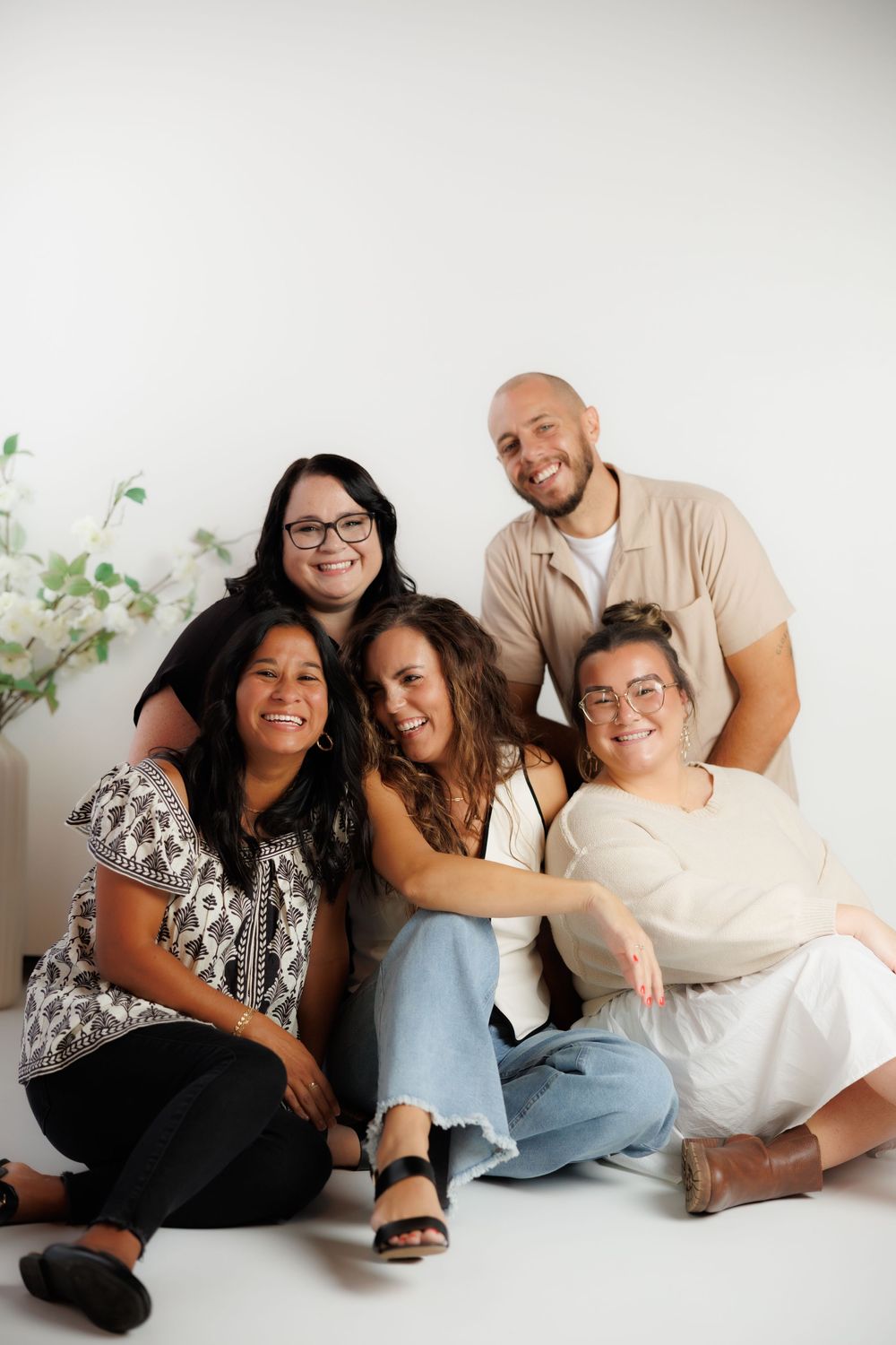 A group lounges together casually on a light colored floor wearing coordinated outfits in a modern indoor setting.