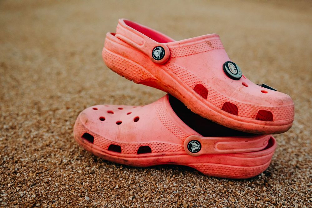 Pair of coral pink Crocs classic clogs stacked on sandy beach ground.