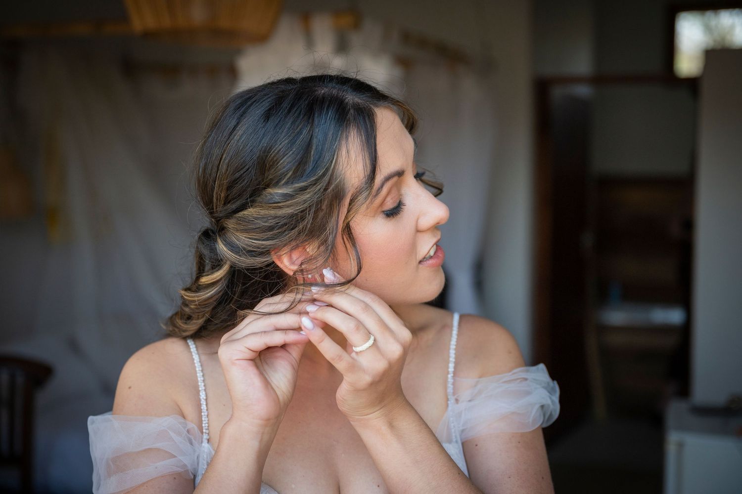 Bride in a white gown and veil poses with ponytail hairstyle against warm indoor lighting.