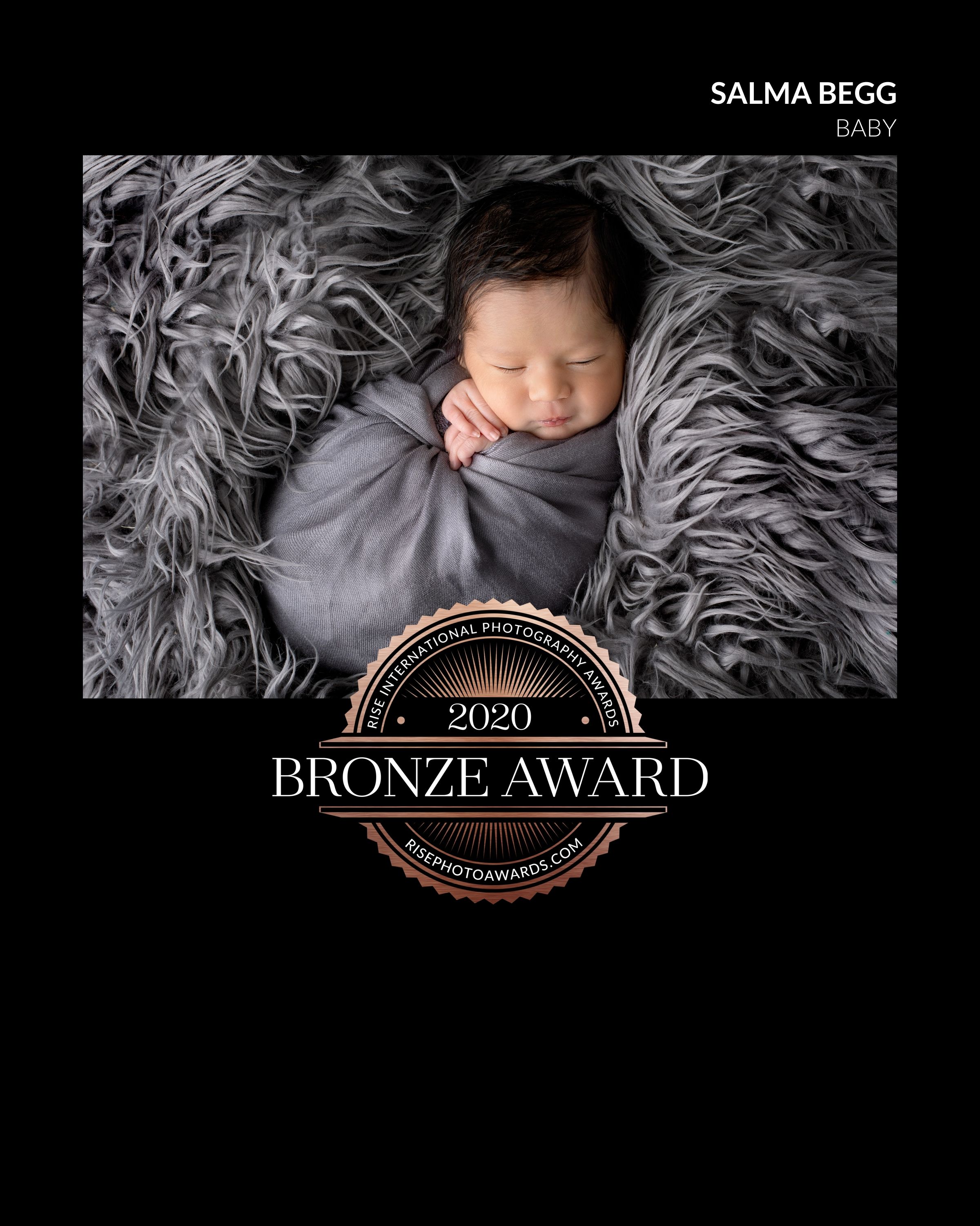 A sleeping newborn baby wrapped in gray fabric lying on fluffy gray fur, with a bronze award badge overlay. ipswich, brookwater, baby photog