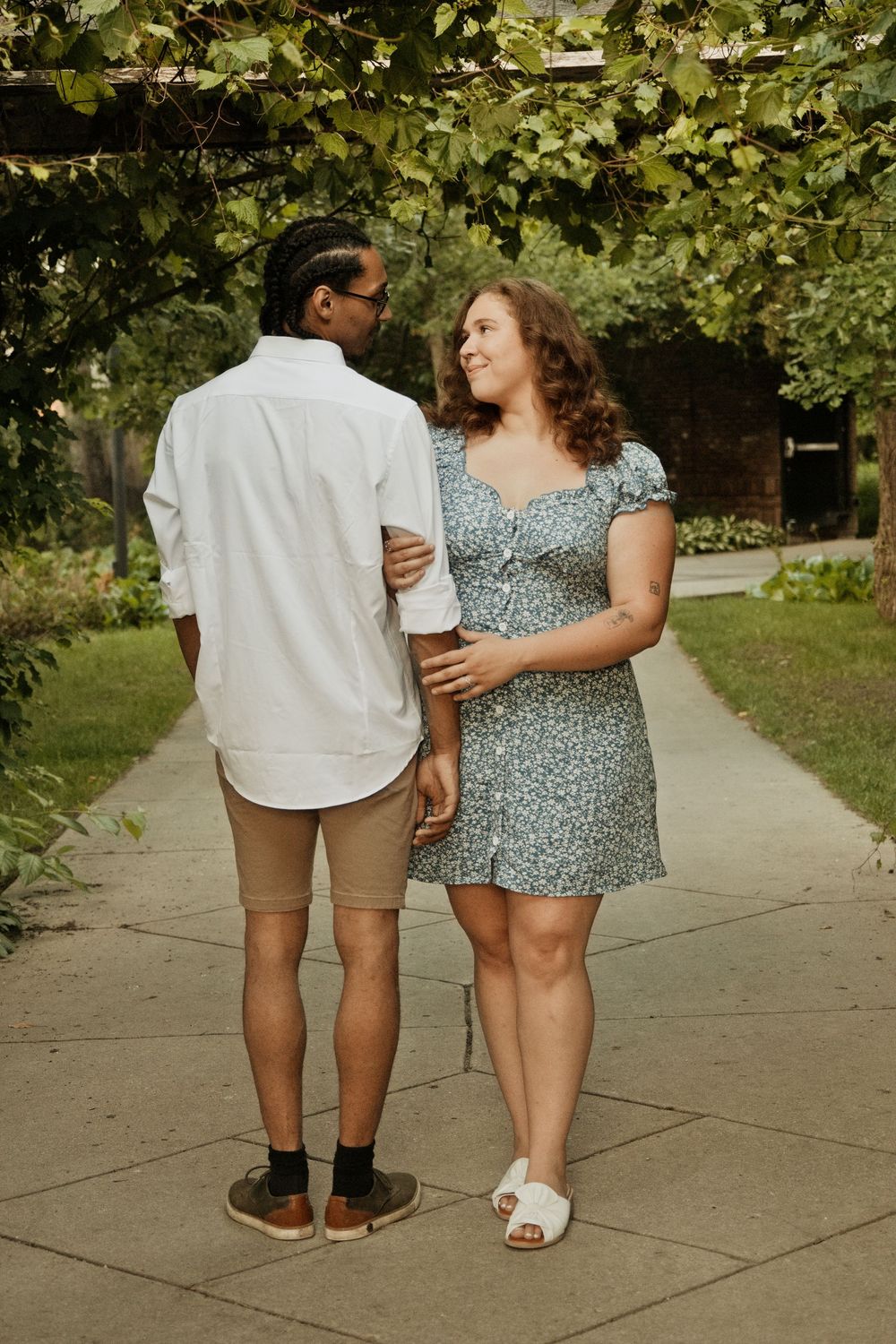 Couple embracing on a garden path, woman in floral dress smiling at man in white shirt and khaki shorts.