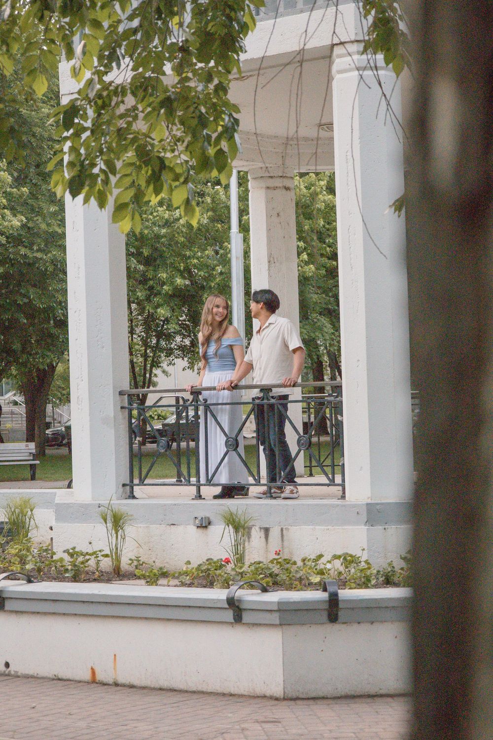 Couple talking on a white gazebo with columns in a lush green park.
