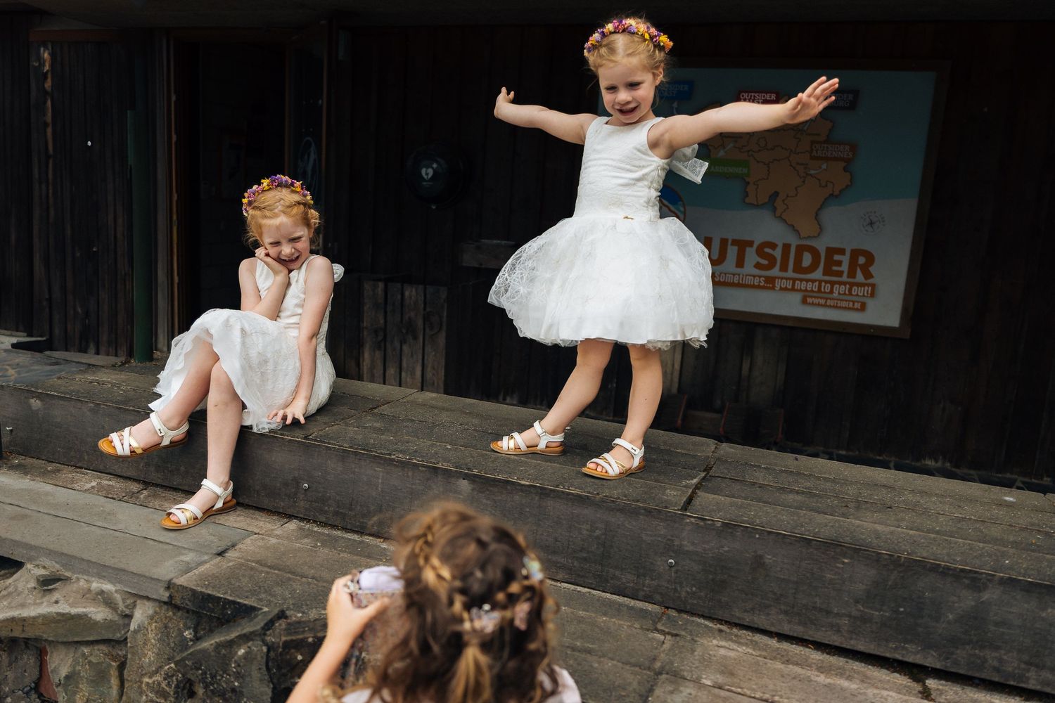 Children in white dresses playing and jumping on wooden steps outdoors.