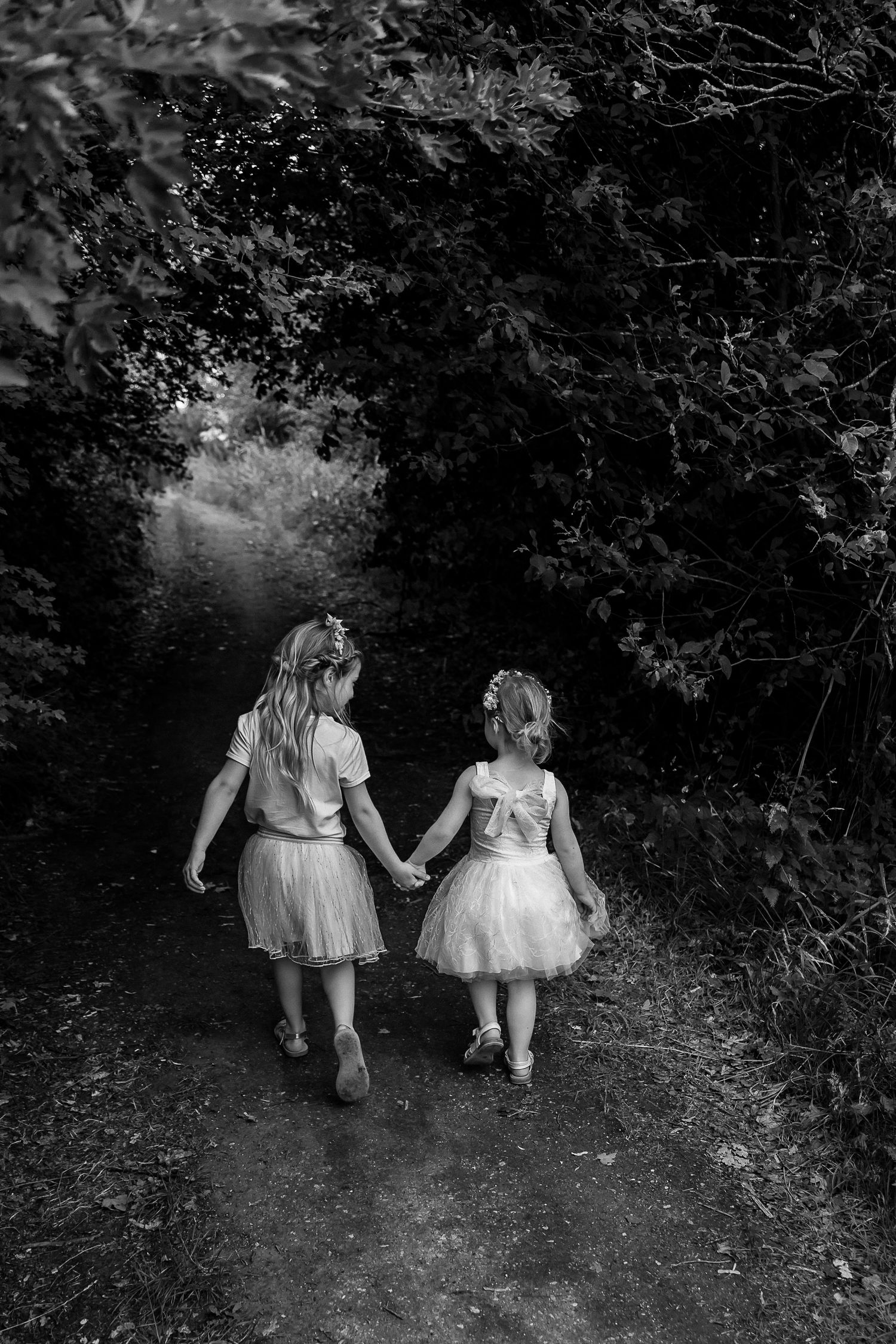 Two children holding hands while walking down a shaded forest path.