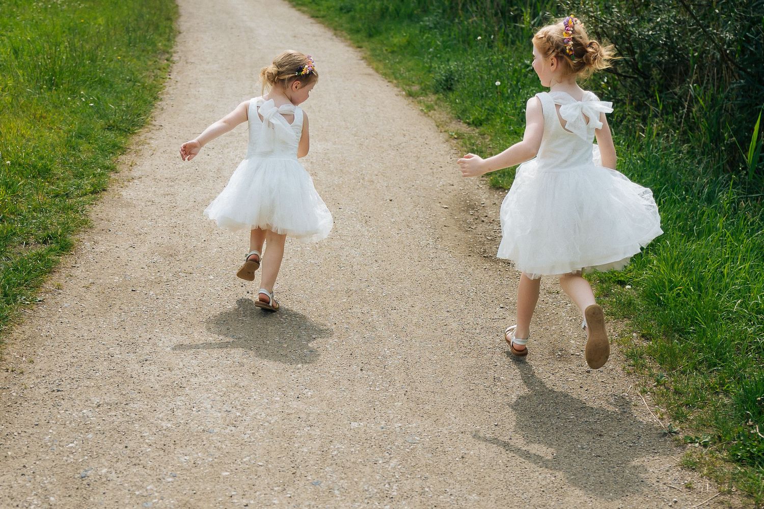 Two children in white dresses running down a countryside path.