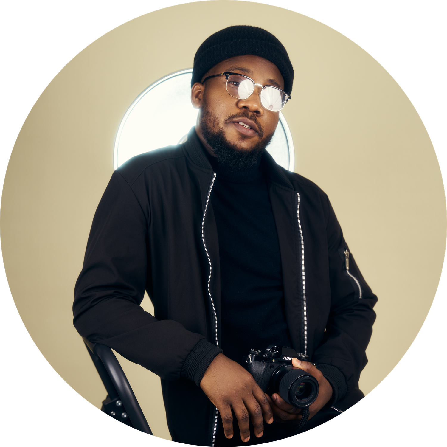 Professional photographer in black attire poses with camera equipment in studio setting.