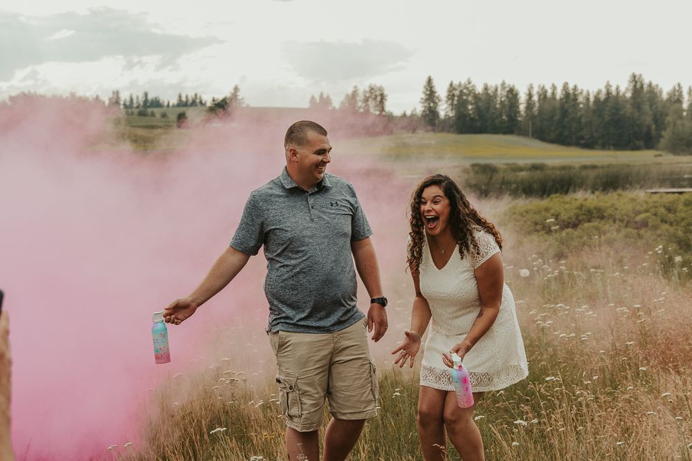 Celebrating gender reveal with pink powder smoke bombs in open field at outdoor photography venue in Spokane, Spokane family photographer