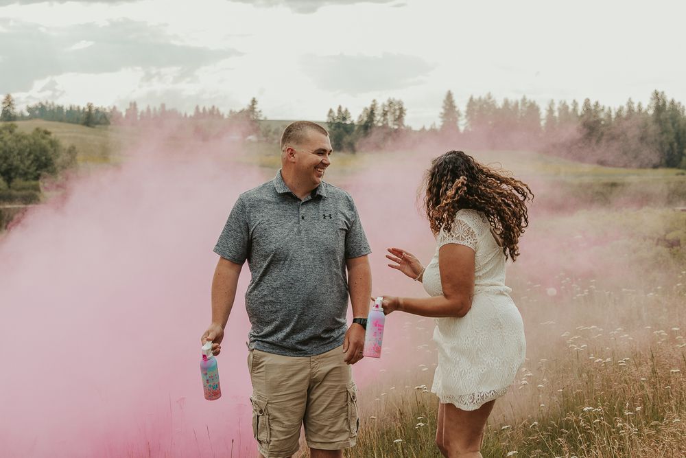 Celebrating gender reveal with pink powder smoke bombs in open field at outdoor photography venue in Spokane, Spokane family photographer