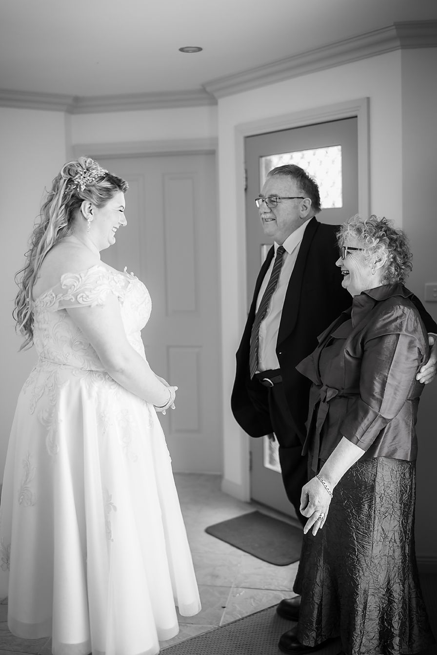 Black and white photo of a couple greeting the bride in her white wedding dress in an elegant interior setting.
