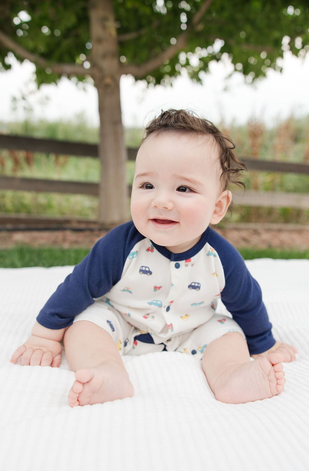 Baby in navy and white outfit lying on blanket outdoors with trees in background.