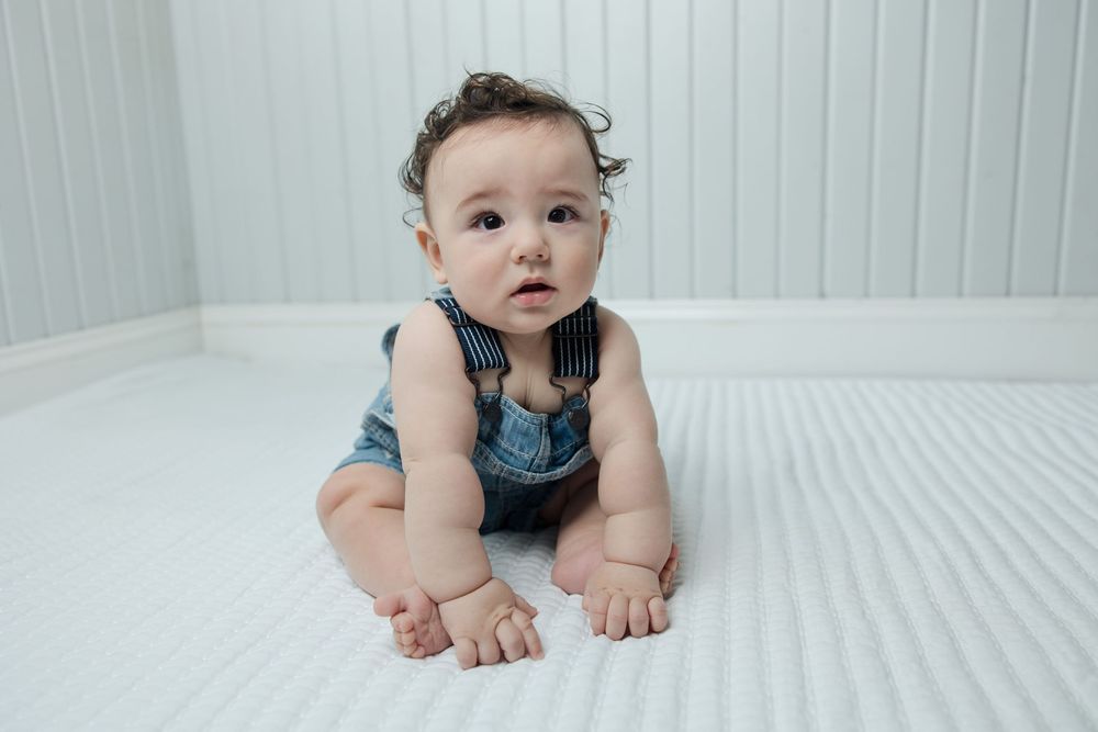 Baby in denim overalls lying on white bedding showing various playful poses.
