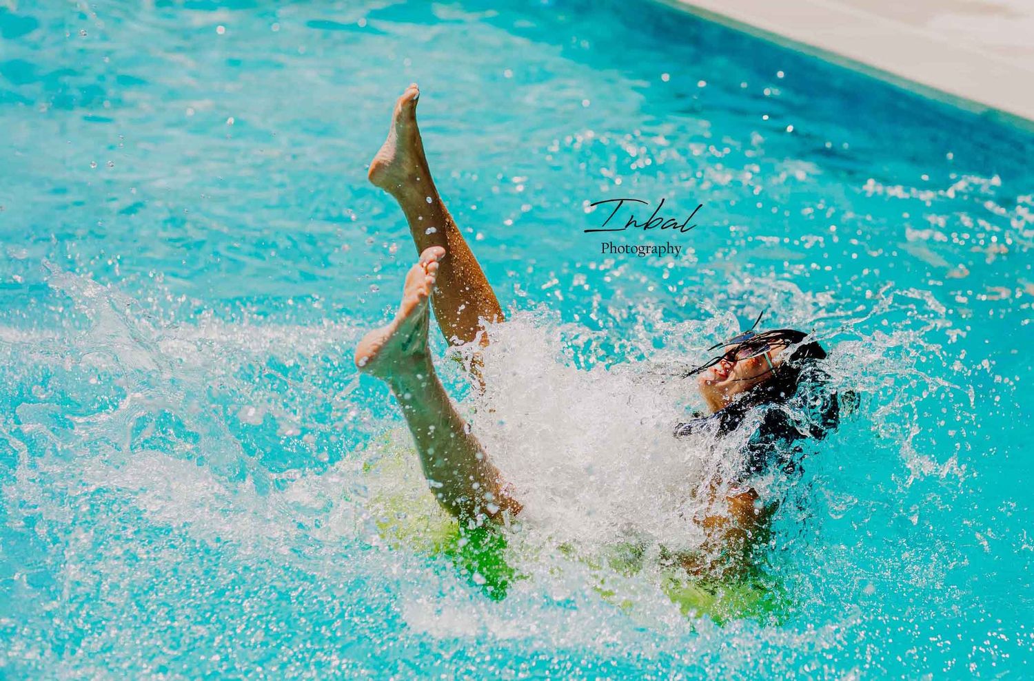 A woman joyfully splashing in a swimming pool while sitting on a green inflatable float during a summer lifestyle photoshoot in Marbella.