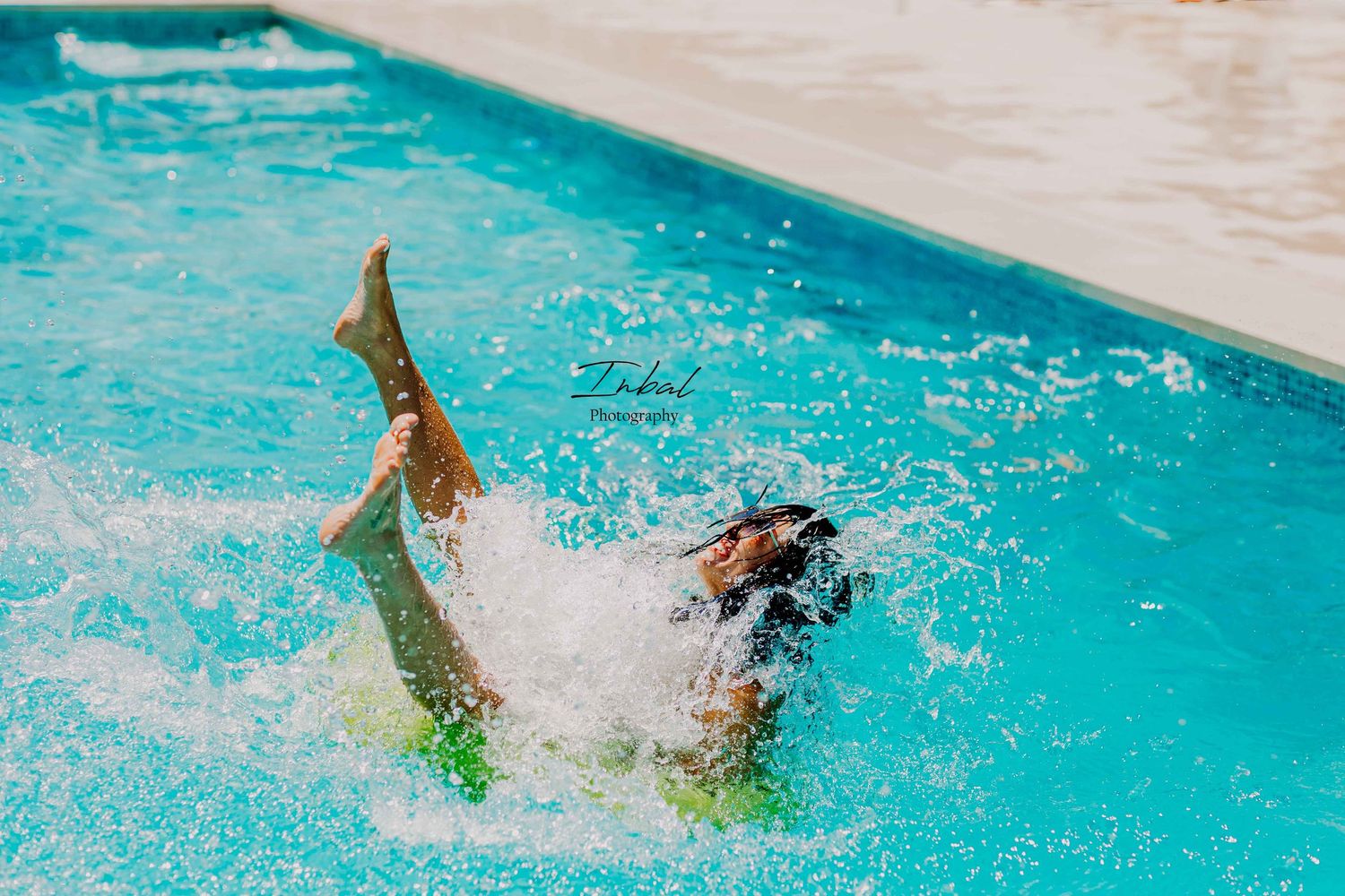 A woman joyfully splashing in a swimming pool while sitting on a green inflatable float during a summer lifestyle photoshoot in Marbella.