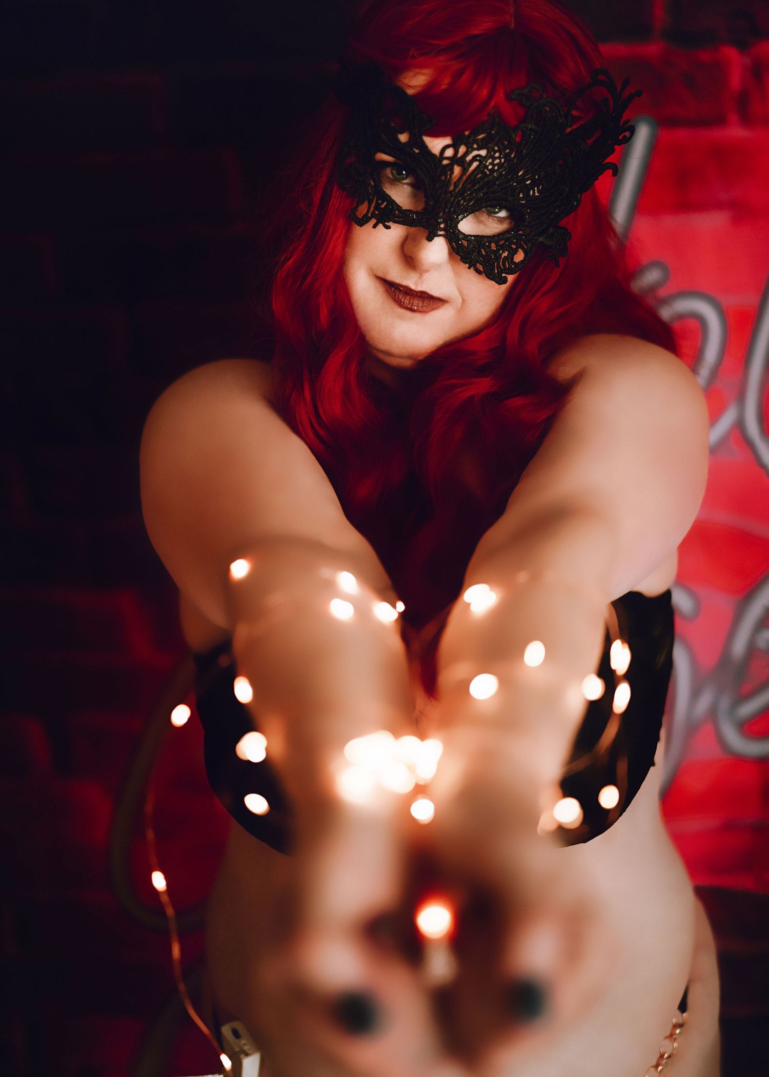 Artistic portrait against red lighting with a black lace mask creating a dramatic and mysterious atmosphere.