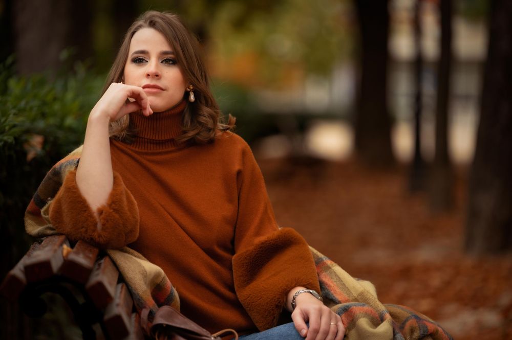 Cozy fall fashion portrait featuring brown sweater amidst autumn leaves and natural outdoor lighting.