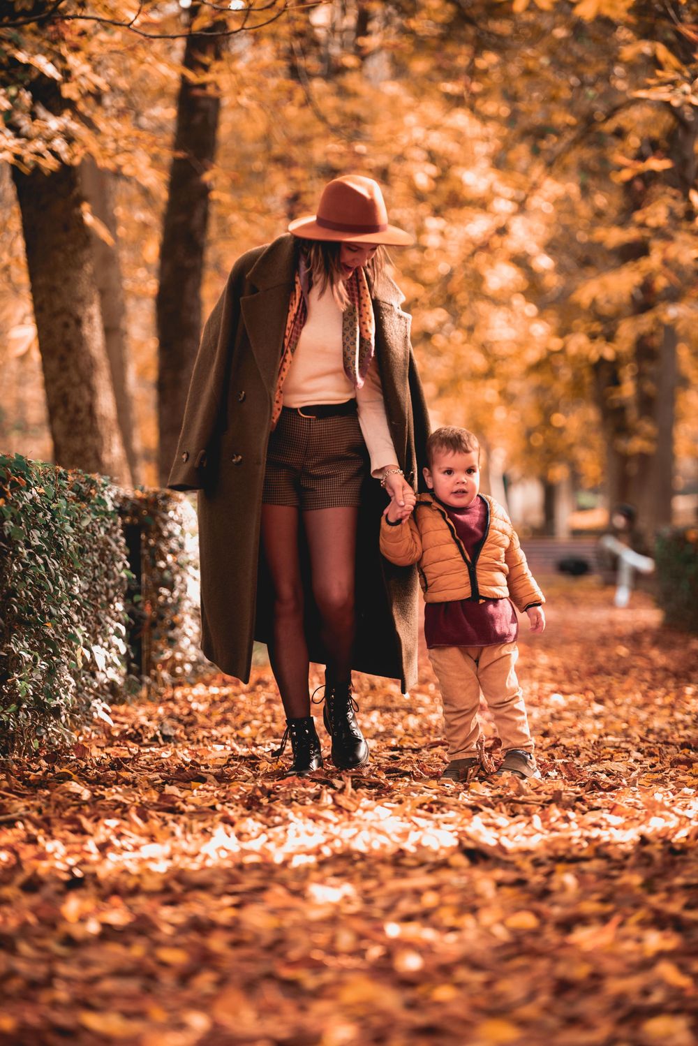 People walking together through a scenic autumn park pathway covered in fallen orange leaves.