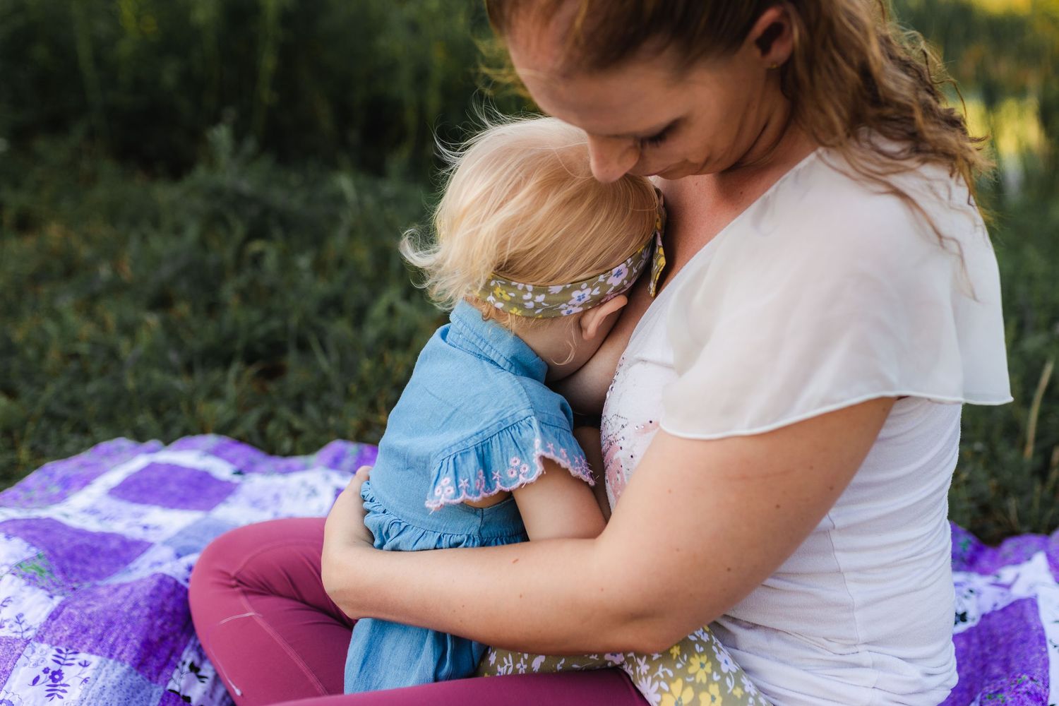 A tender moment between parent and child sitting on a purple blanket outside in nature during golden hour.