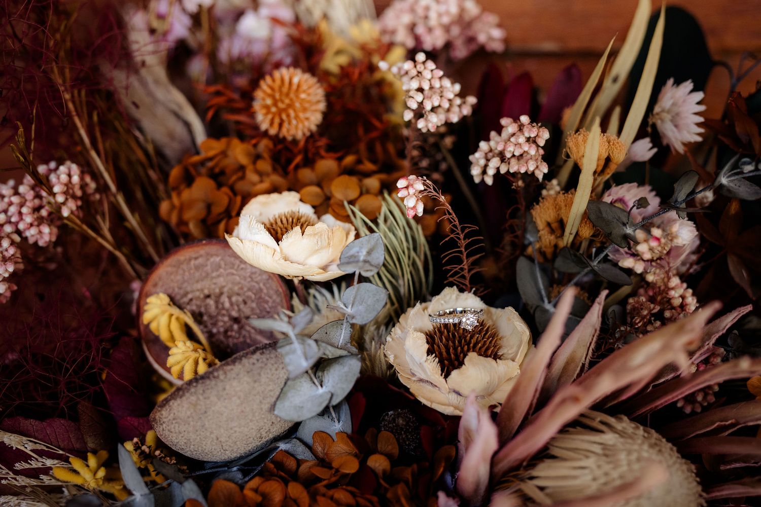 Close-up of moody floral arrangement with white ranunculus, dried flowers, and muted pink blooms in warm lighting.