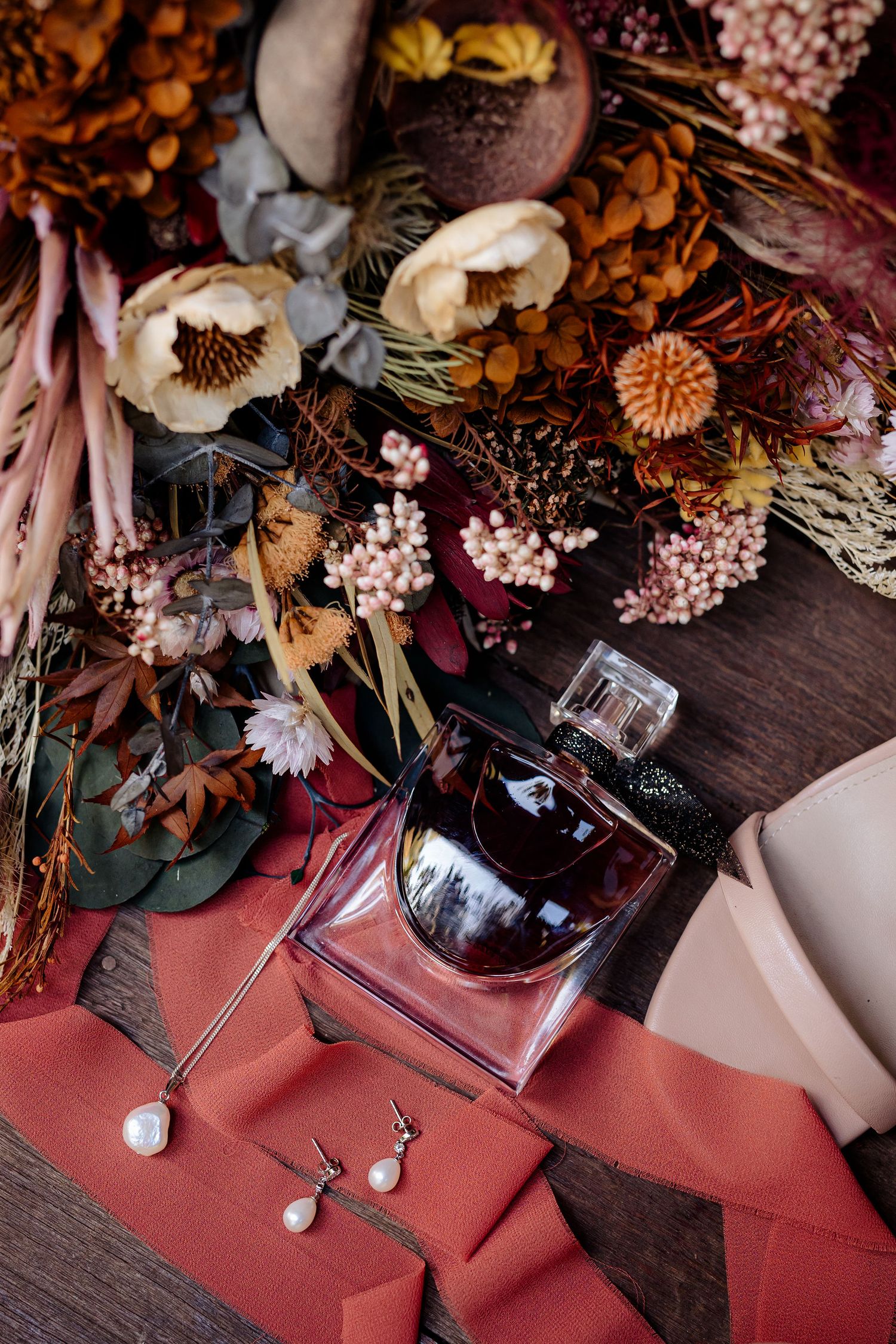 Artfully arranged dried flowers and vintage perfume bottles displayed on rustic wooden surface with red accent decor.