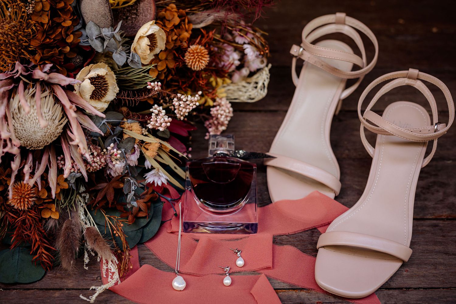 Wedding details featuring floral arrangements, bridal accessories, and pink accents against a rustic wooden background.