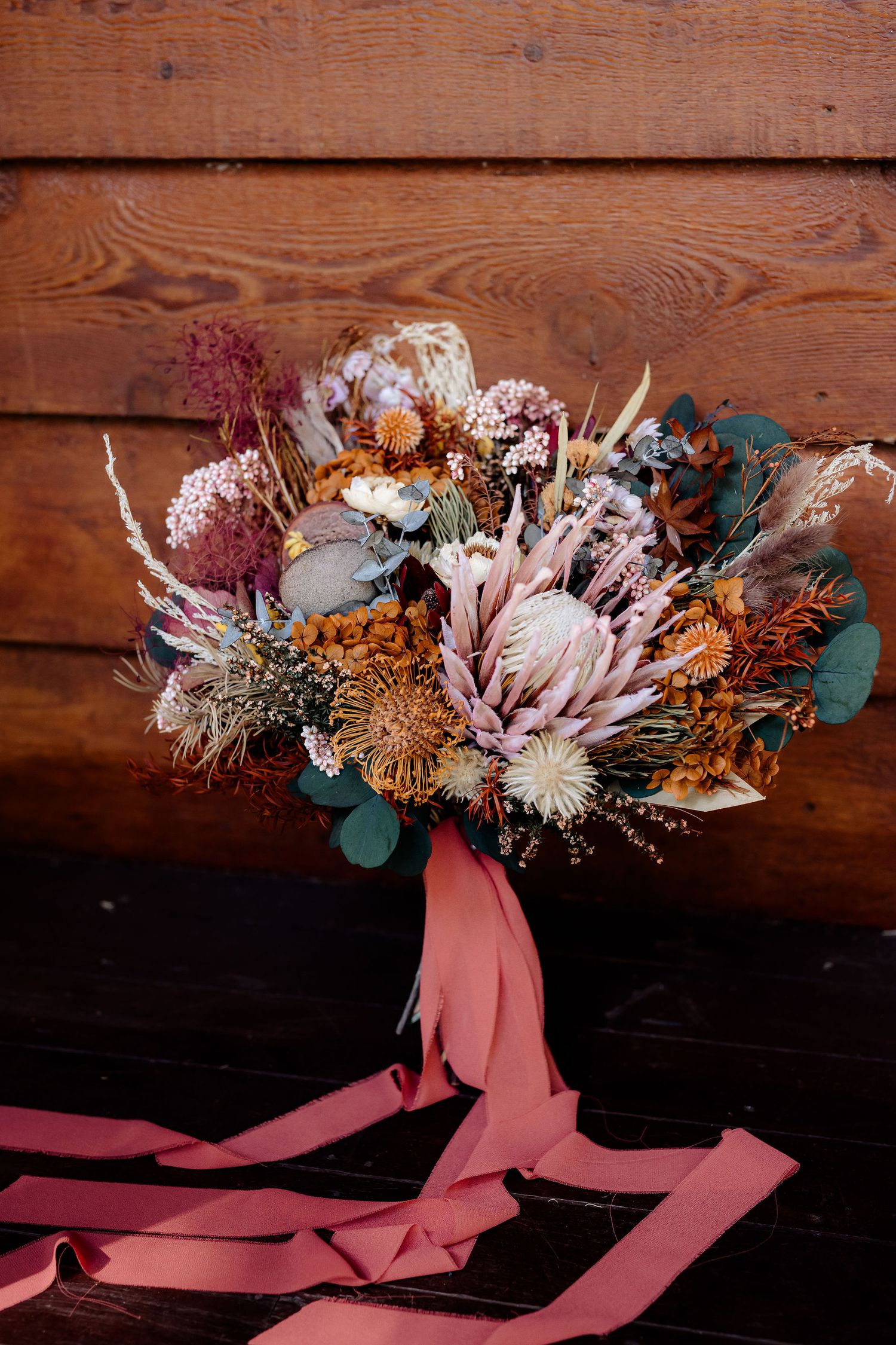 Rustic wedding bouquets with dried flowers tied with pink ribbons arranged against wooden backdrop for autumn decor.