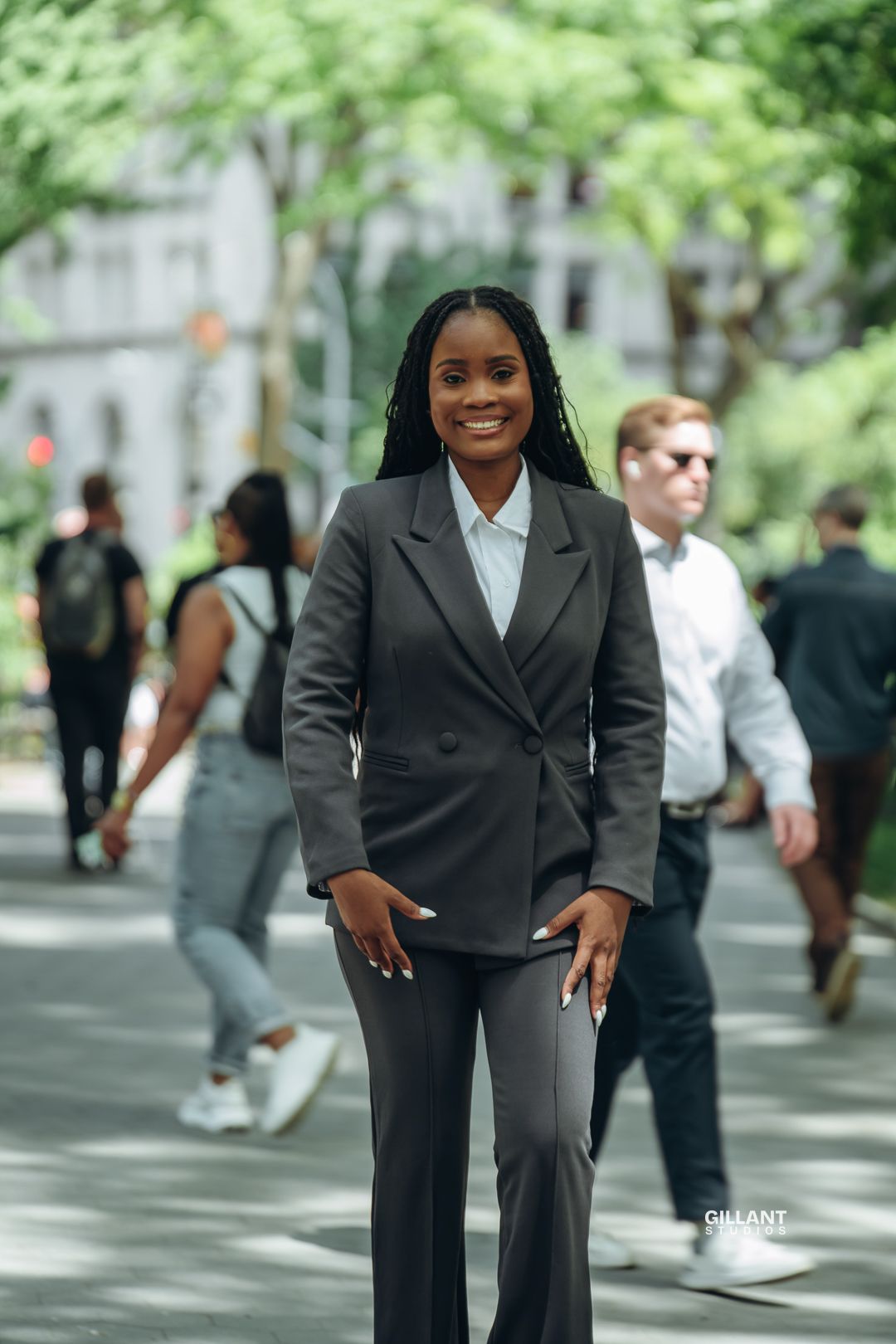 Professional in dark business suit stands confidently on tree-lined city street.