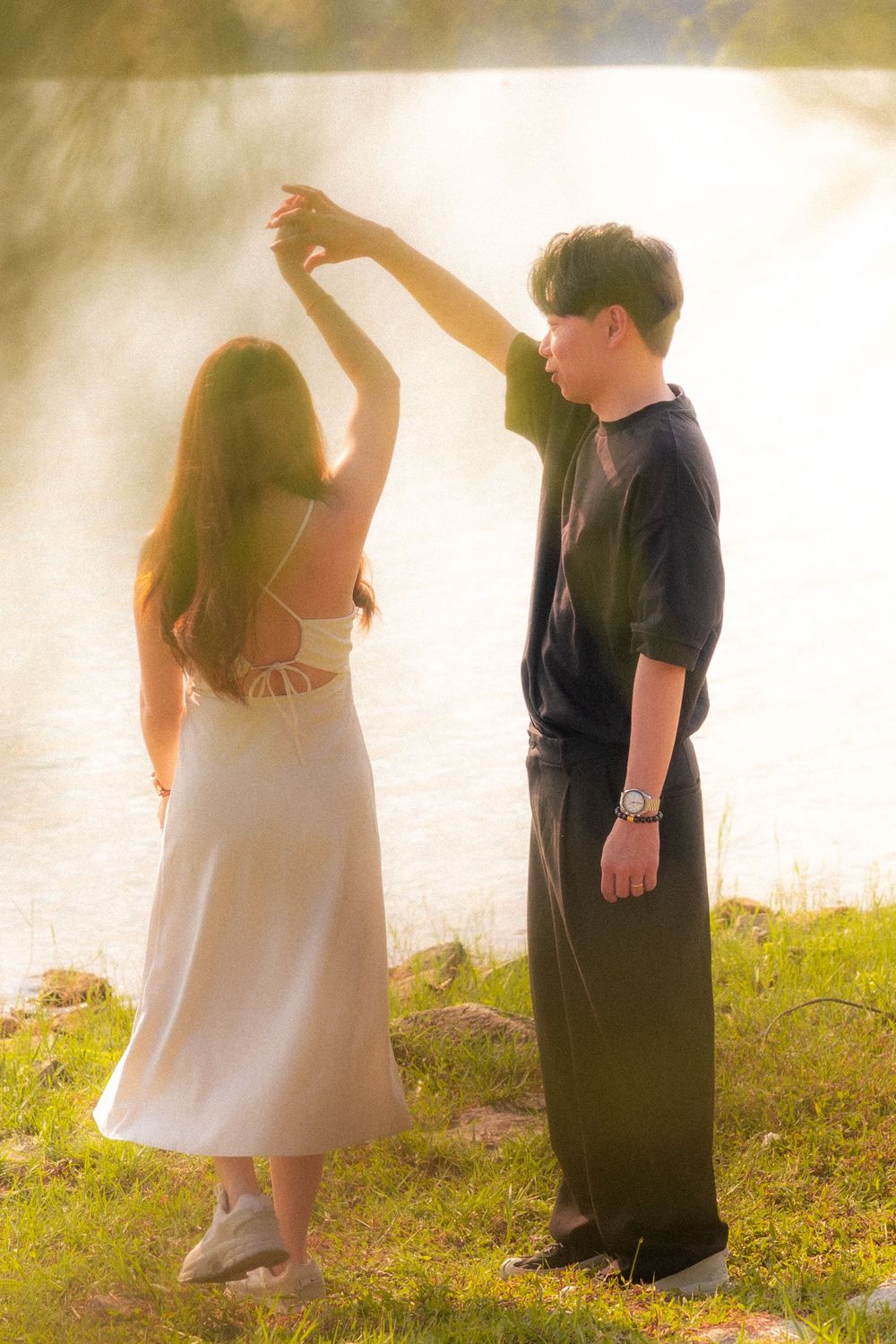 A couple holding hands and dancing together in a dreamy golden sunset by a lake.